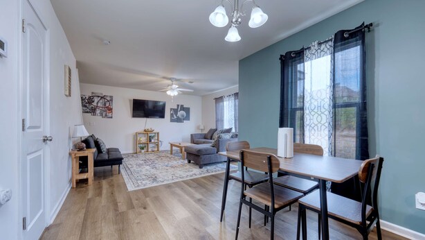 A spacious living area with a dining table, chairs, a sofa, a ceiling fan, and a large window with curtains. - Pet-Friendly House Near Ft Benning w/ Free Parking (Columbus)
