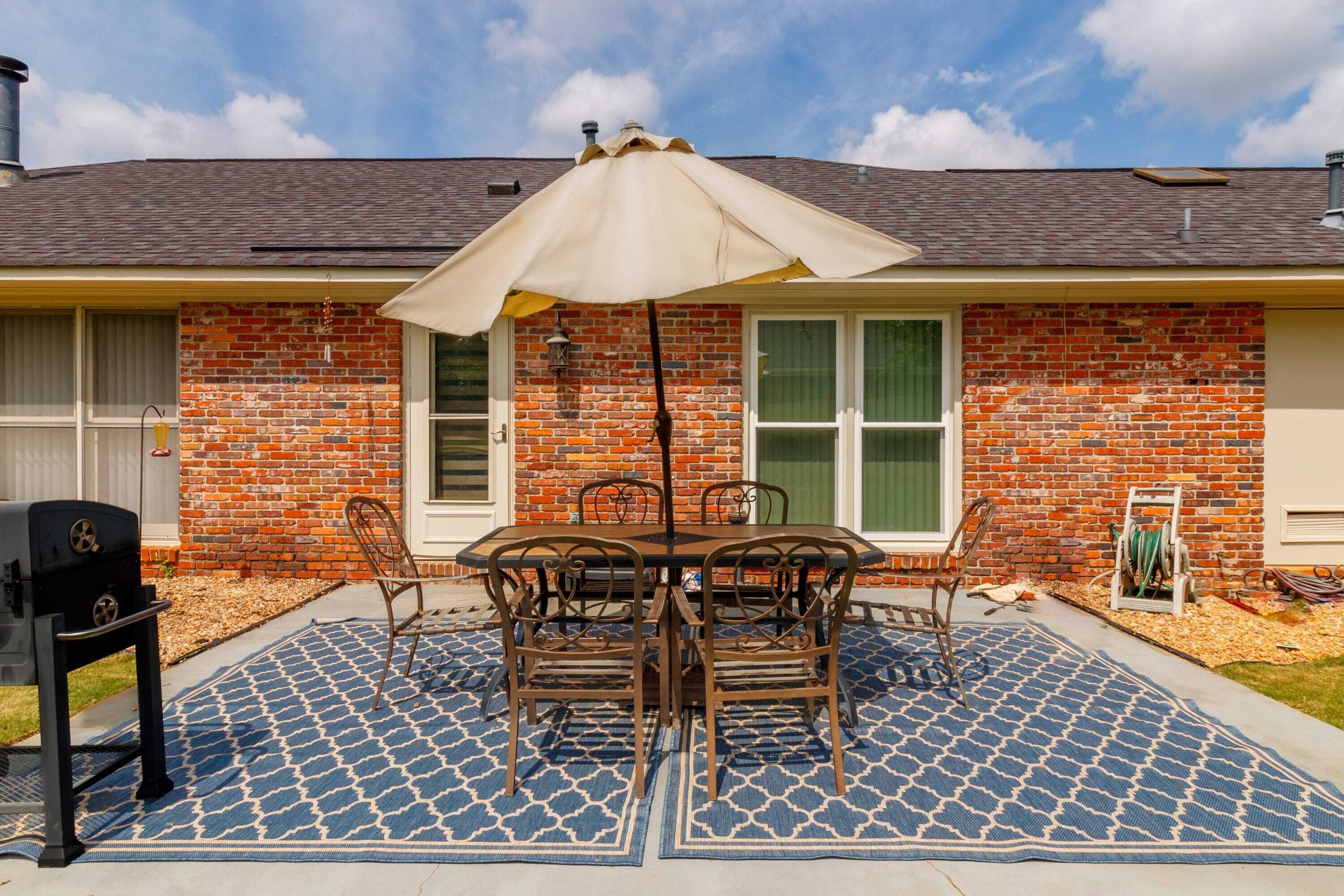 A patio with a table and chairs, a grill, and a covered umbrella.
