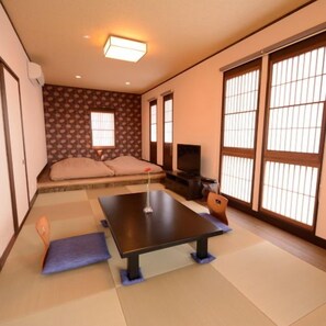 A traditional Japanese room with tatami flooring, a low table, cushions, sliding doors, and a television. - Izukogen Hanairotei (Ito)