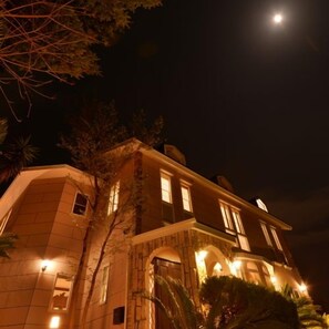 A two-story building with a stone facade, multiple windows, and a moon in the sky. - Izukogen Hanairotei (Ito)