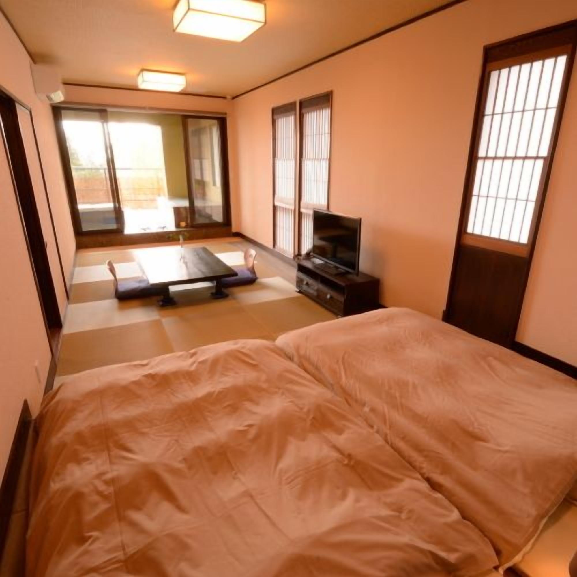 A traditional Japanese room with tatami flooring, a futon bed, sliding doors, and a television.