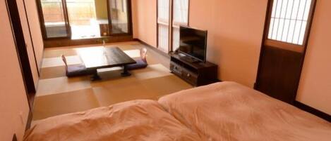 A traditional Japanese room with tatami flooring, a futon bed, sliding doors, and a television.