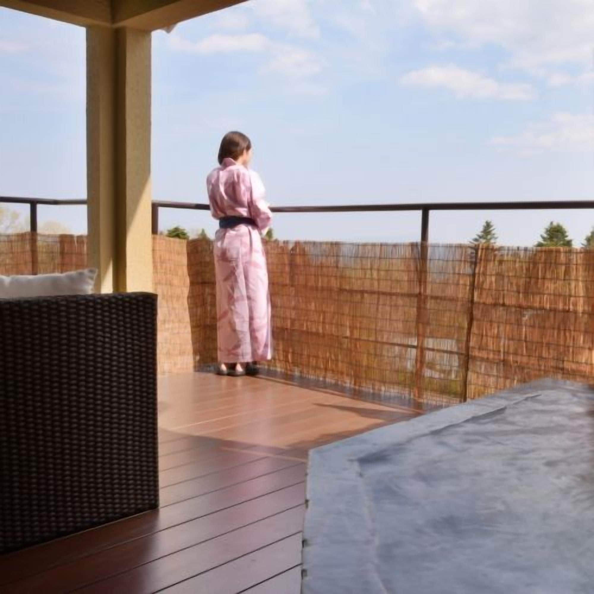 A person standing on a wooden deck with a view of a bamboo fence and trees.
