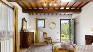 A bedroom with a bed, a wooden dresser, a chair, a mirror, and a view of the outdoors. - Spacious Double Room Surrounded by Nature (Vicchio)