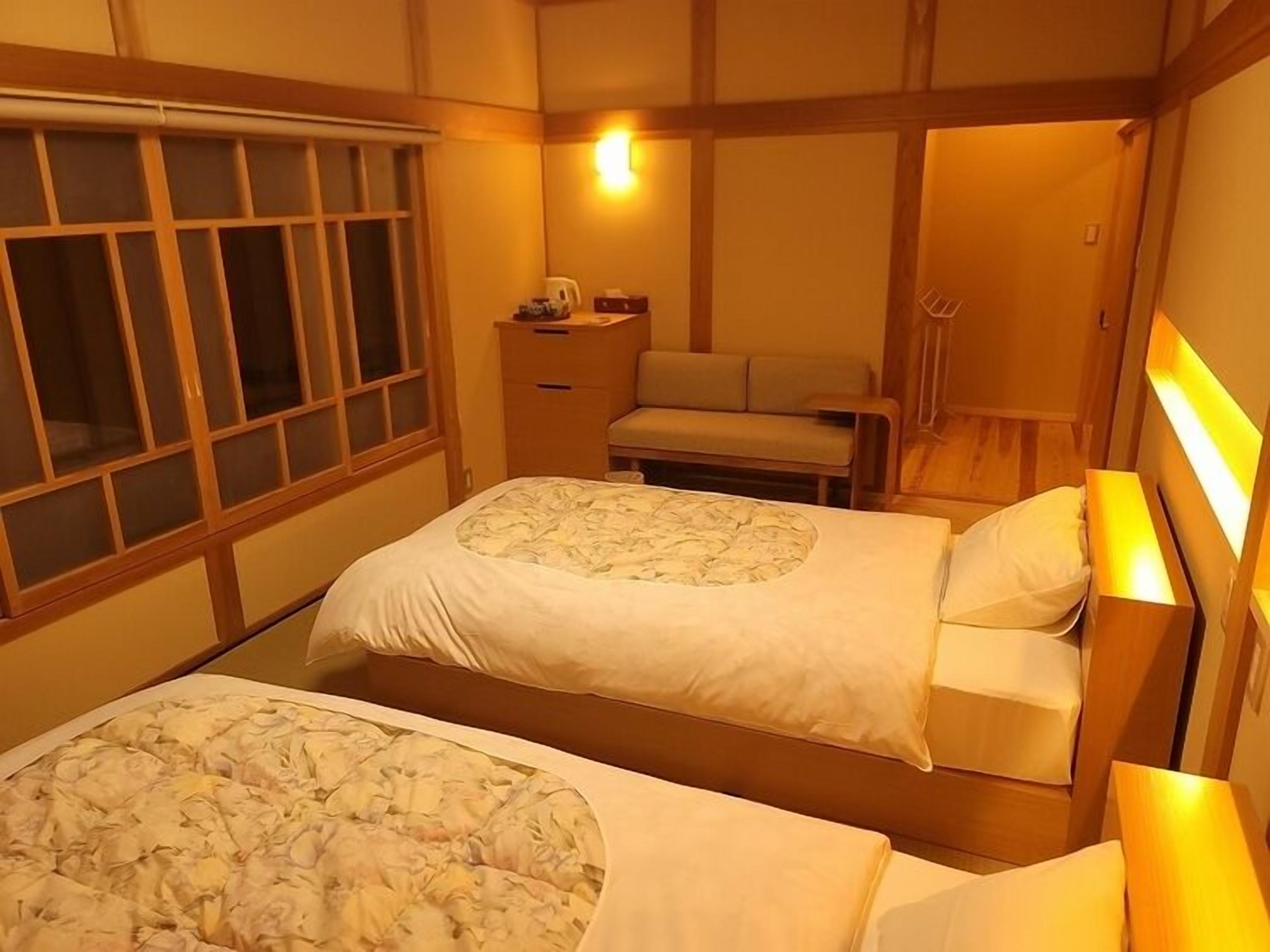 Habitación de hotel con dos camas, una mesita de noche, un escritorio y una ventana con persianas.