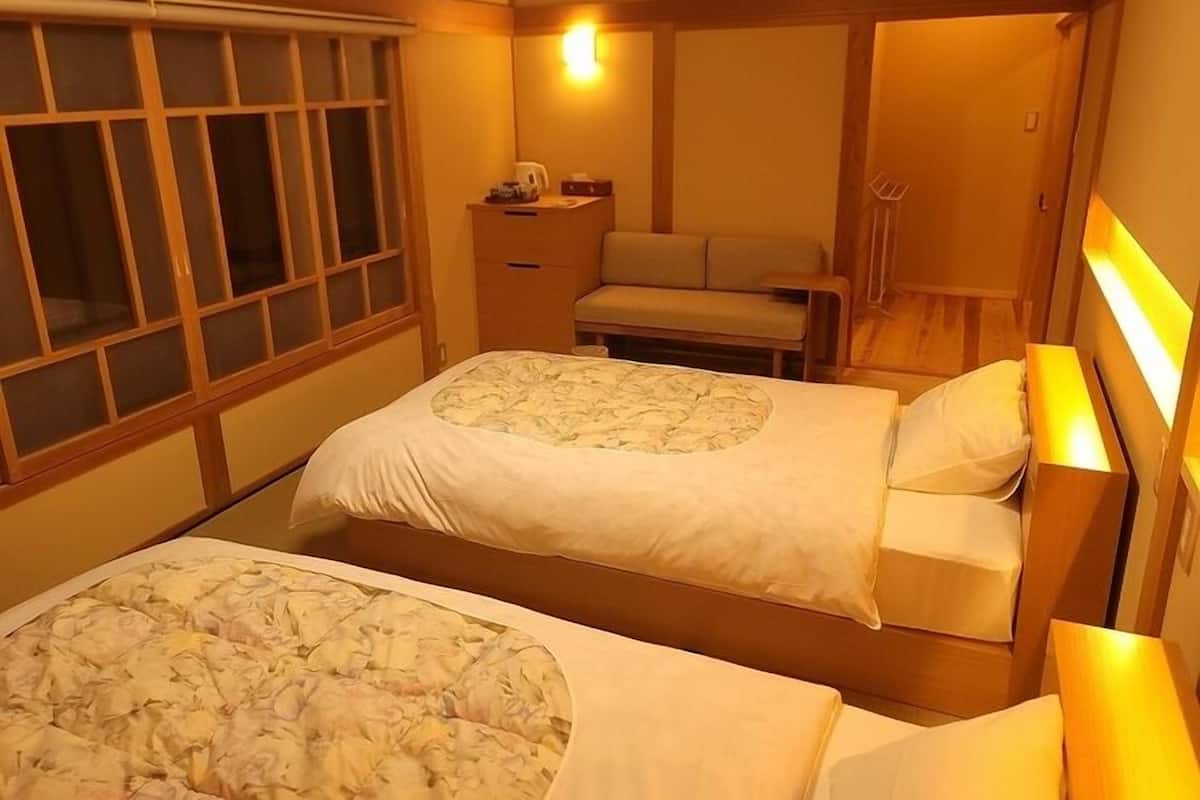 A hotel room with two beds, a nightstand, a desk, and a window with blinds.