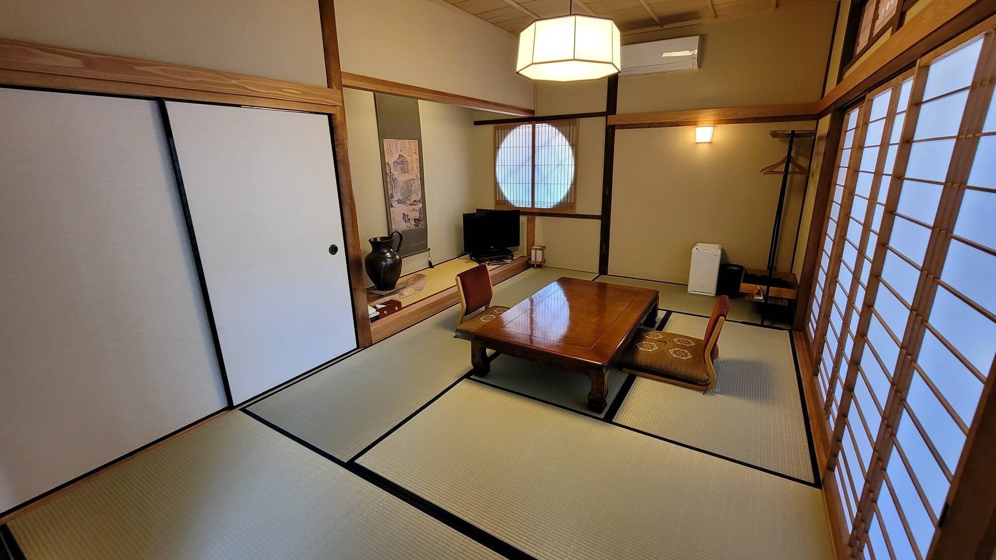 Una habitación japonesa tradicional con suelo de tatami, una mesa baja, un televisor y una puerta corredera.