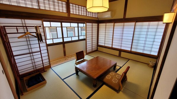A traditional Japanese room with tatami flooring, a low wooden table, a cushioned bench, and sliding doors with a grid pattern.
