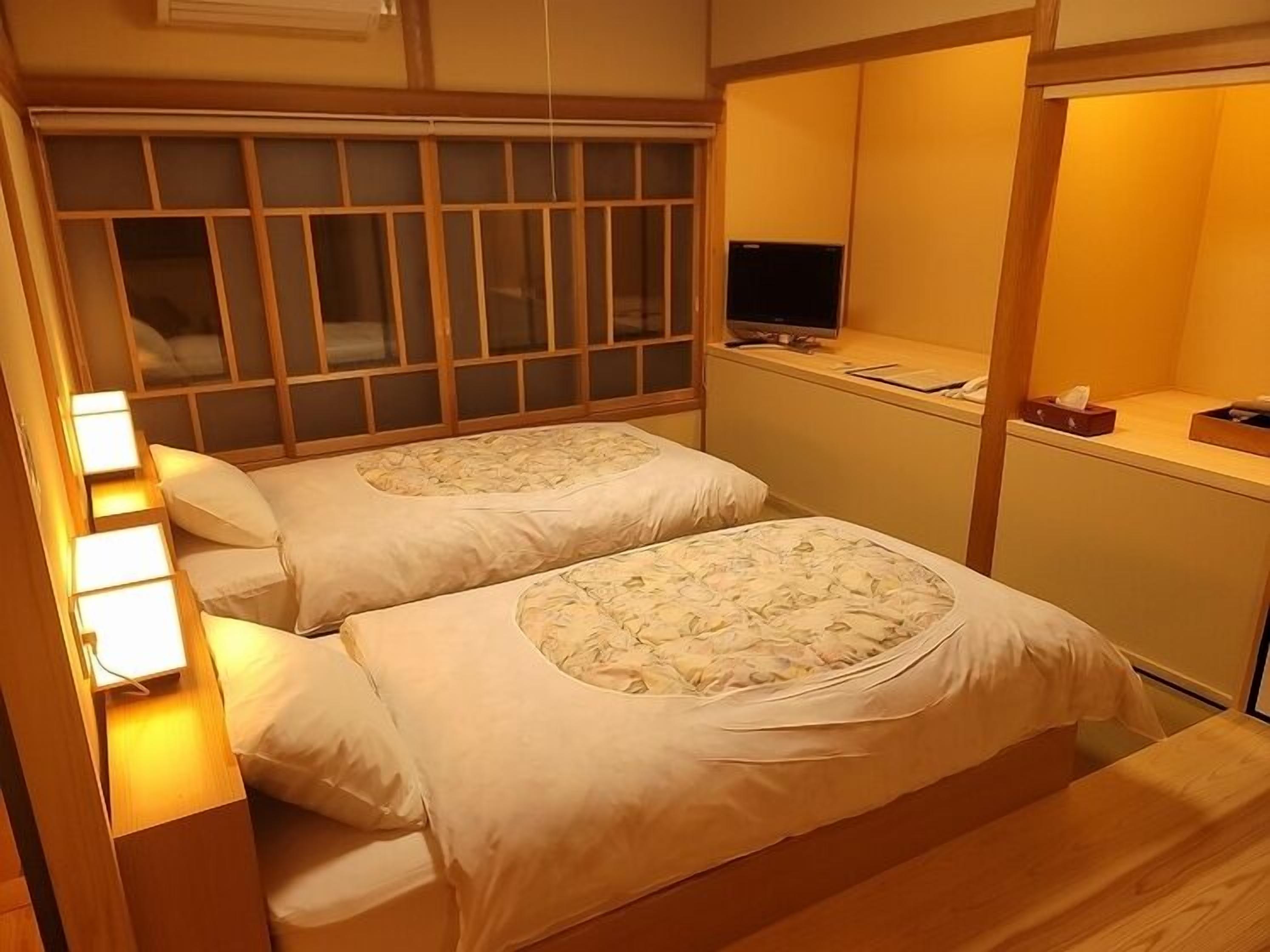 Una habitación con dos camas, televisión y un escritorio pequeño con lámpara.