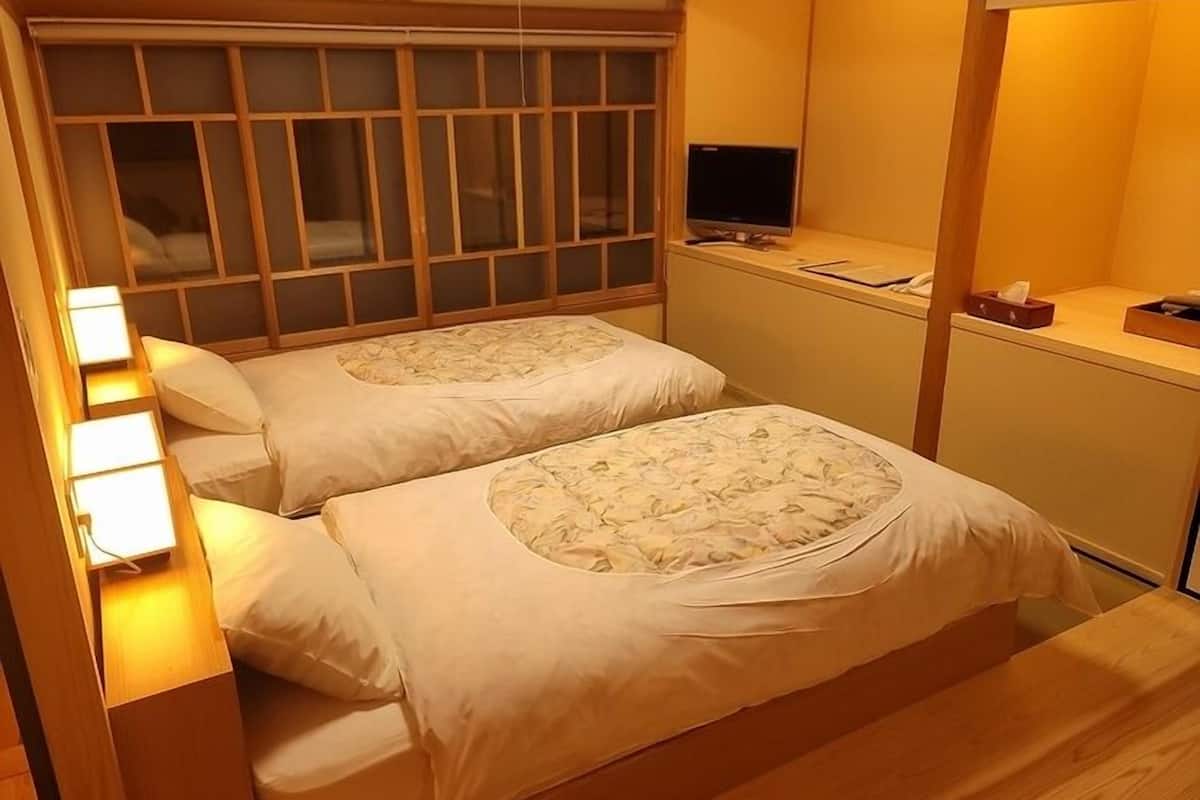A room with two beds, a TV, and a small desk with a lamp.