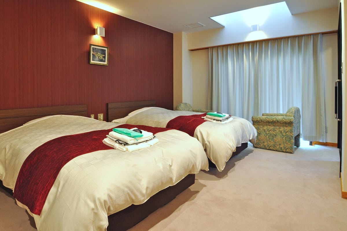 A hotel room with two beds, a chair, a desk, and a window with curtains.