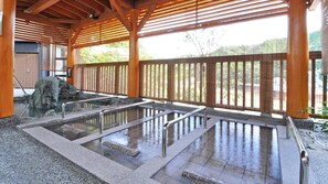 Un onsen japonais traditionnel, avec des bains en pierre, des poutres en bois et une vue sur le paysage environnant.