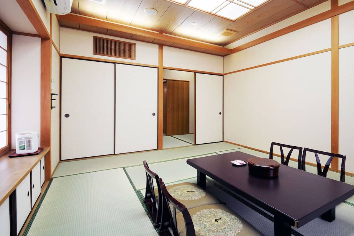 A traditional Japanese room with tatami flooring, a low table with chairs, and sliding doors.