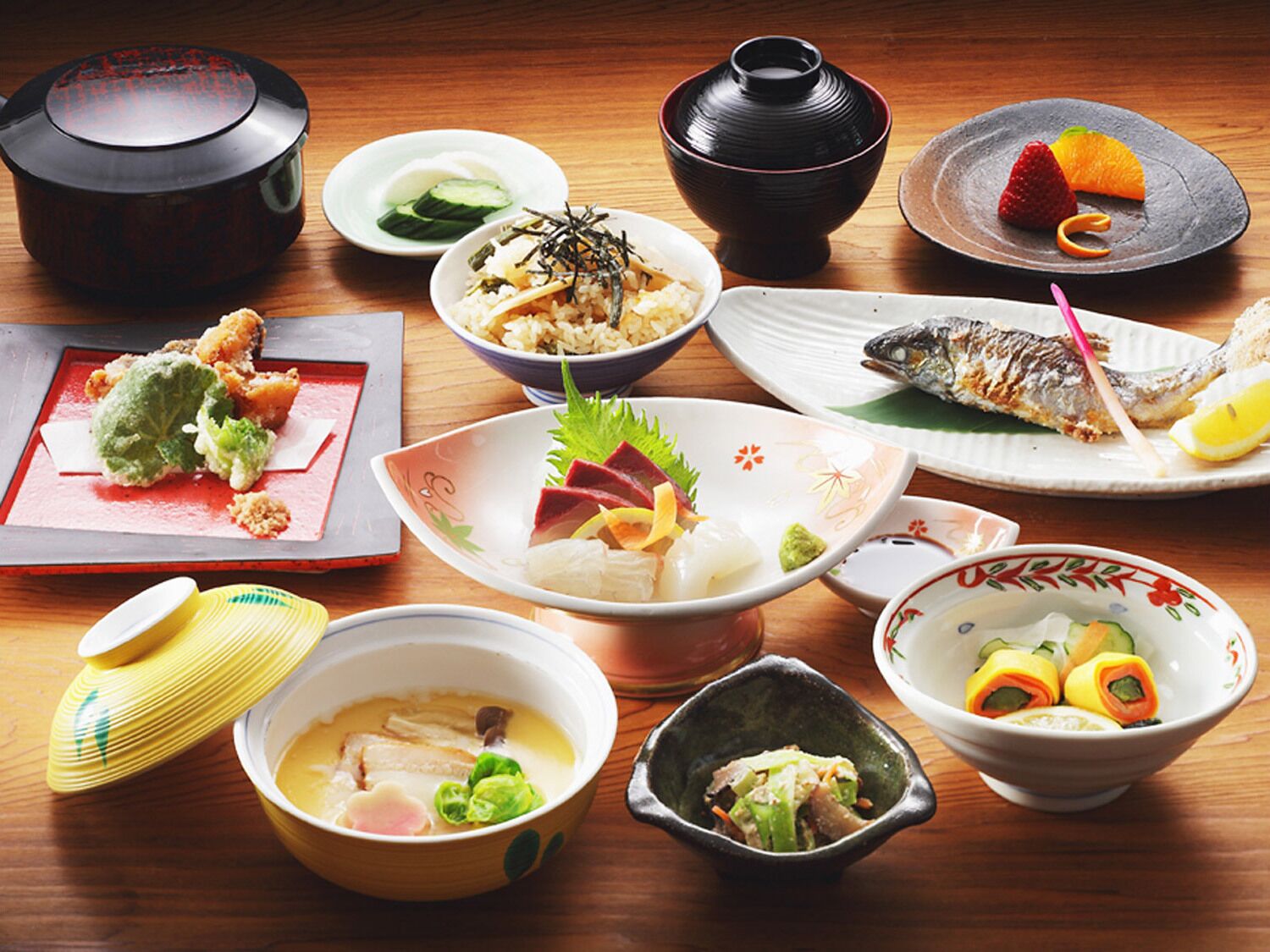 A variety of dishes on a wooden table, including sushi, sashimi, and a bowl of soup.