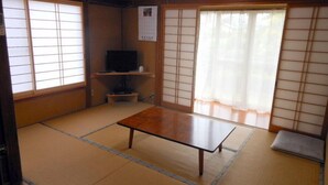 Ein traditioneller japanischer Raum mit Tatami-Boden, einem niedrigen Tisch, Schiebetüren und einem Fernseher.