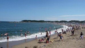 Ein überfüllter Strand mit badenden und flanierenden Personen.
