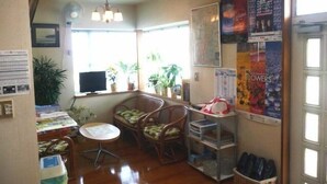 A room with a dining table, chairs, a small round table, a fan, a television, and a window with plants. - Mansyuya (Hitachinaka)