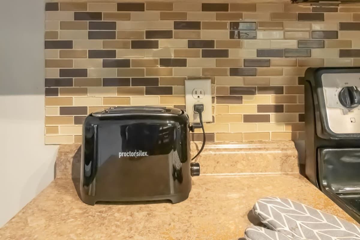 A kitchen with a toaster on the counter, a tiled backsplash, and a power outlet.