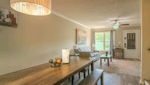 Ein geräumiges Wohnzimmer mit einer hölzernen Bank, einem Tisch mit Dekoration, einem Deckenventilator und einer Tür, die nach draußen führt.