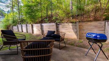 Un jardin avec des chaises en osier, un barbecue et une clôture en bois.