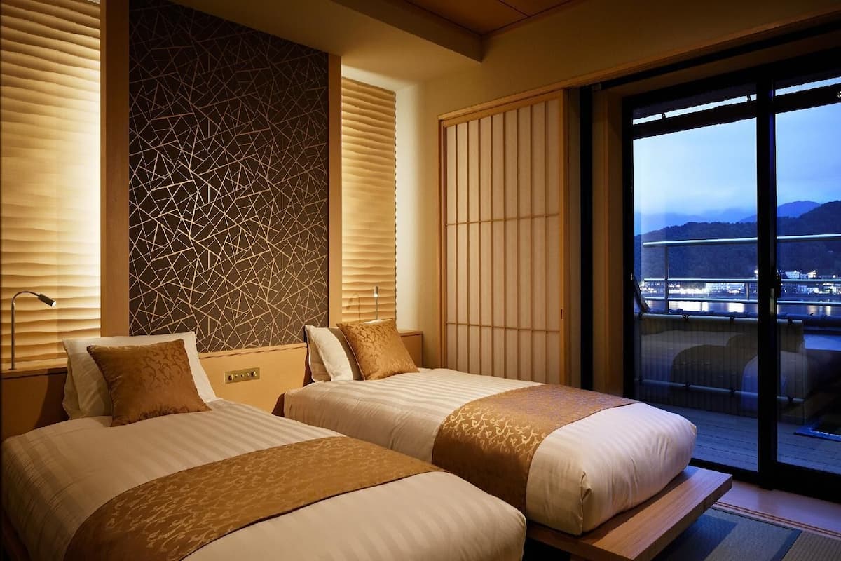 A hotel room with two beds, a view of a cityscape through large windows, and a decorative wall with a geometric pattern.