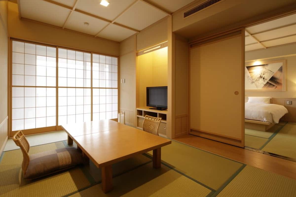 A traditional Japanese room with tatami flooring, a low wooden table, a television, and a bed with a futon.