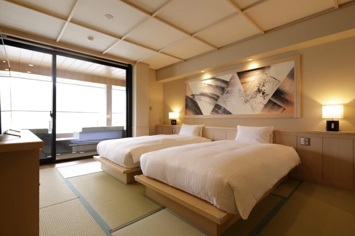 A hotel room with two beds, a large abstract painting, sliding glass doors, and a desk.