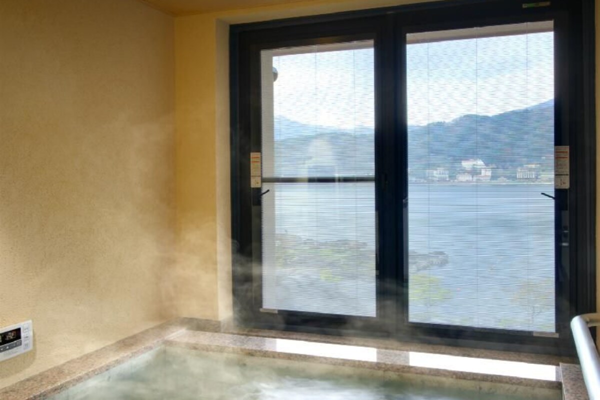 Uma banheira de hidromassagem com vista para a água e montanhas através de uma janela.