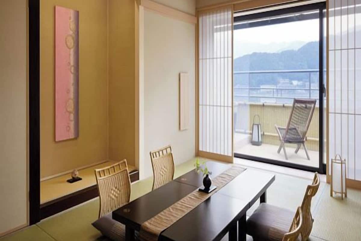 A traditional Japanese room with tatami flooring, a low table, and sliding doors leading to a balcony with a view.