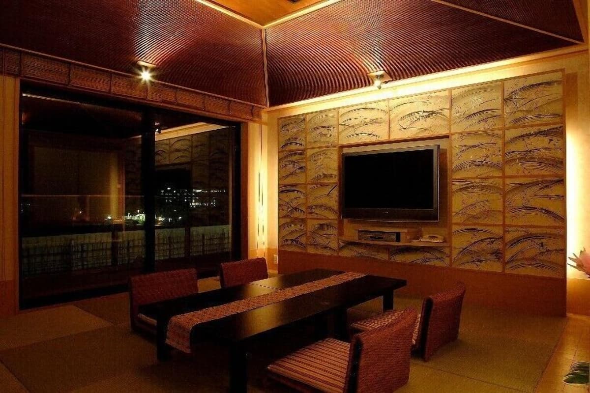 A dining area with a large table and chairs, a flat-screen TV mounted on the wall, and a city view through large windows.