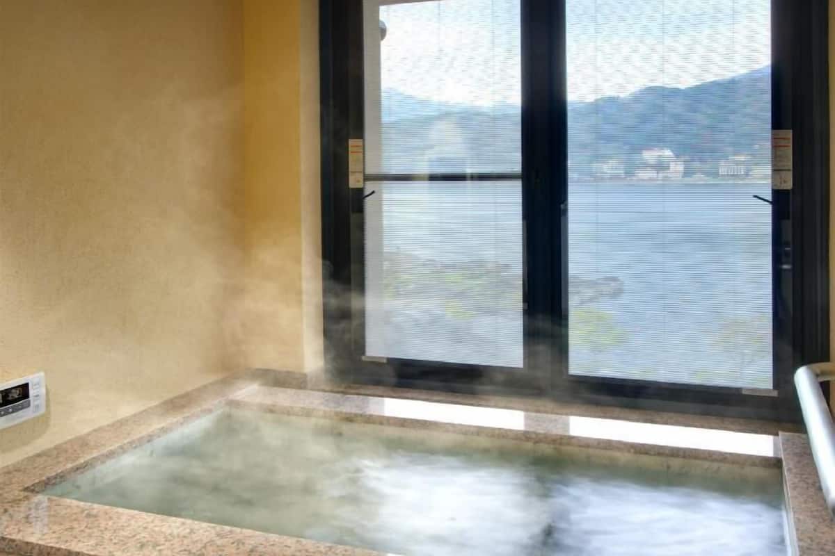 A hot tub with a view of a body of water and mountains through a window.