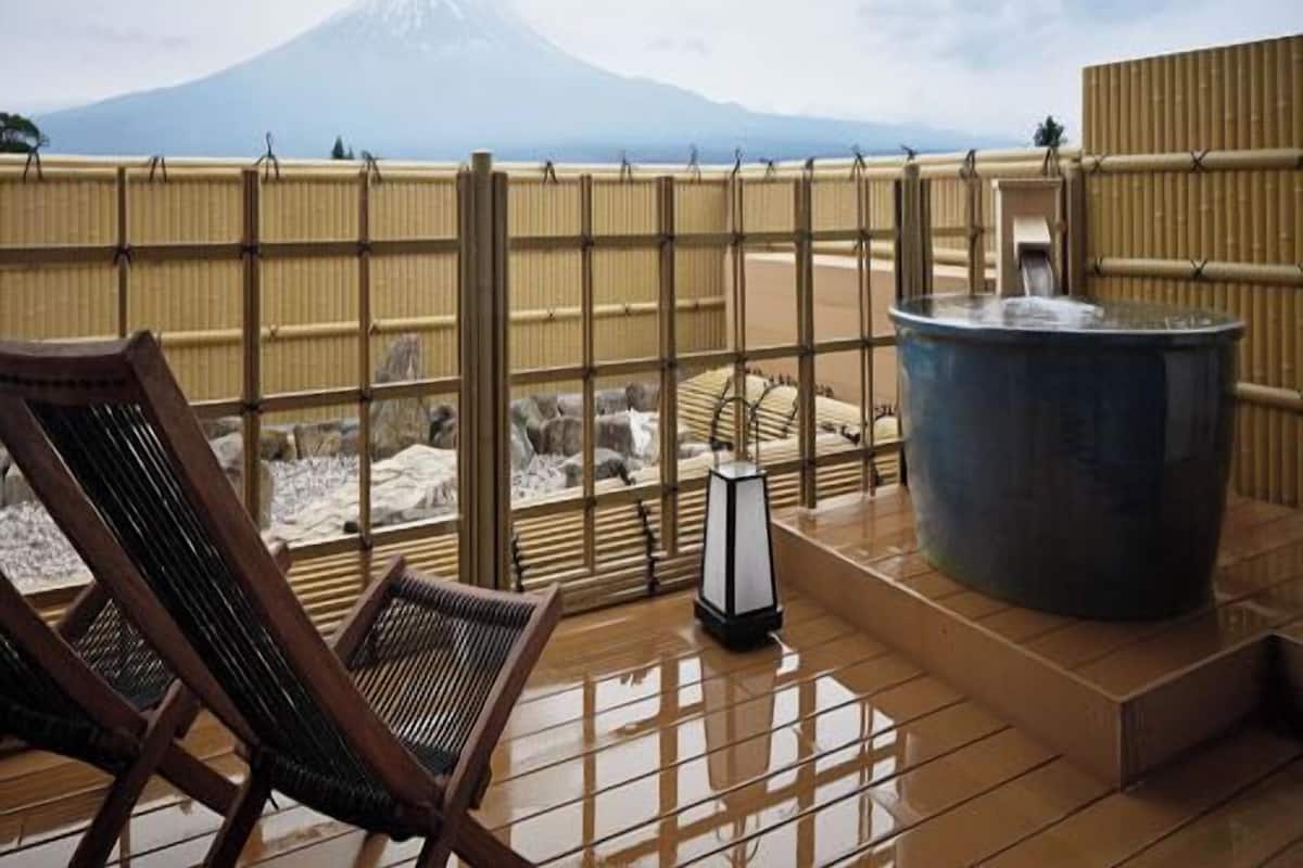 A wooden deck with a hot tub and chairs, overlooking a mountain.