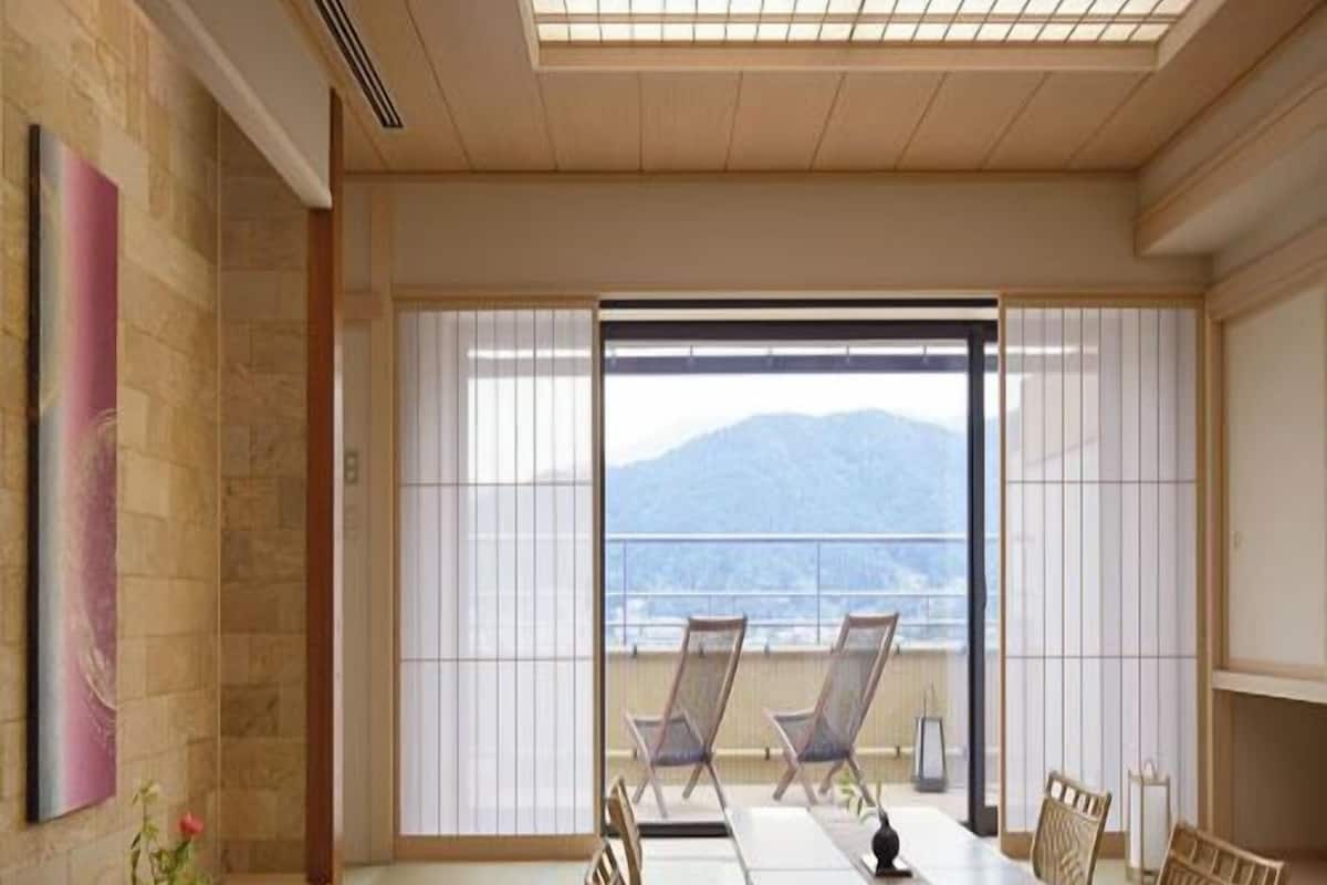 A traditional Japanese room with tatami flooring, a low table with cushions, sliding shoji doors, and a view of mountains.
