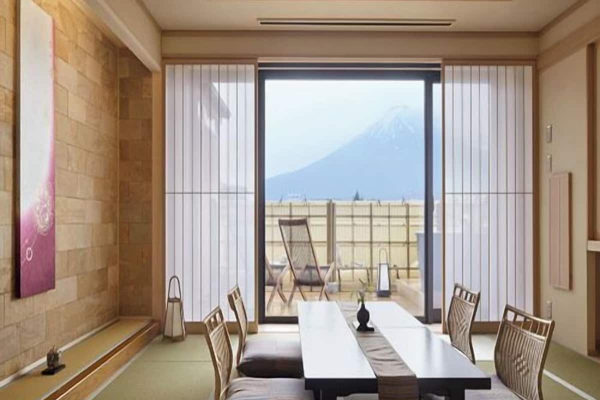A room with a large sliding glass door, a dining table with chairs, and a view of a mountain.