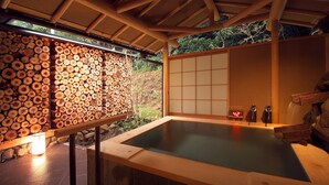 A traditional Japanese onsen with a wooden log wall, a tatami mat room, and a stone hot spring.