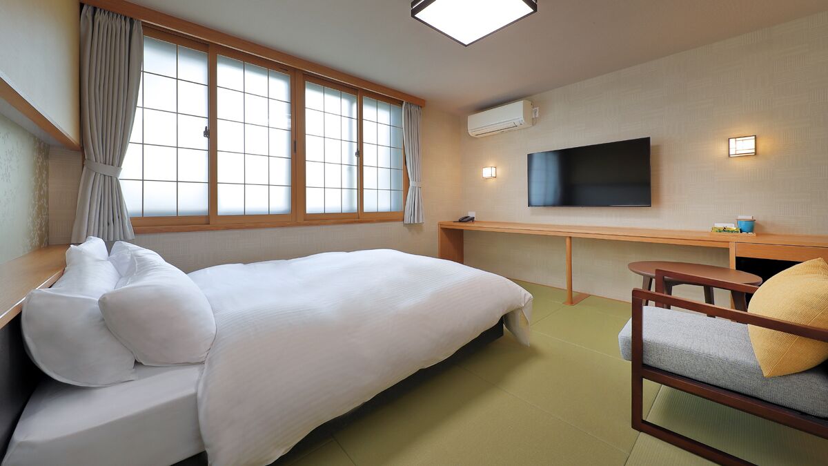 A hotel room with a bed, a desk, a chair, a TV, and a window with curtains.