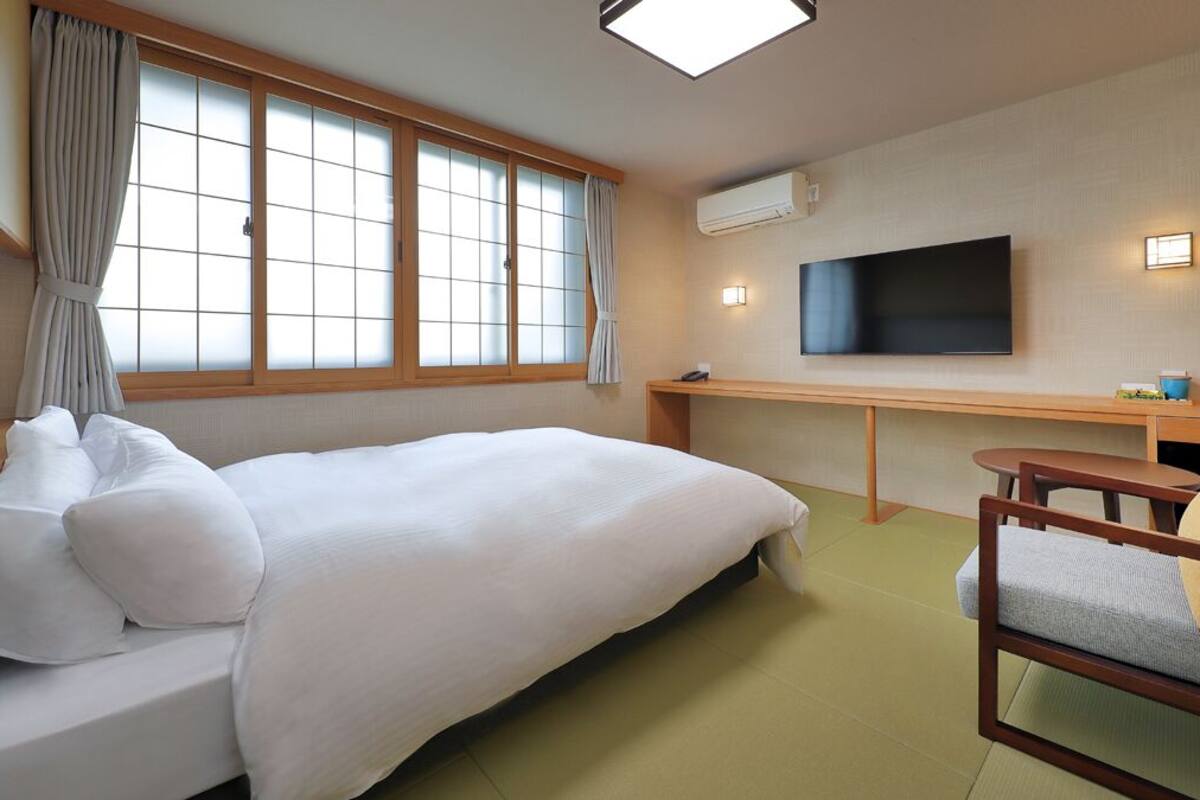Une chambre d’hôtel avec un lit, un bureau, une chaise, une télévision et une fenêtre avec des rideaux.