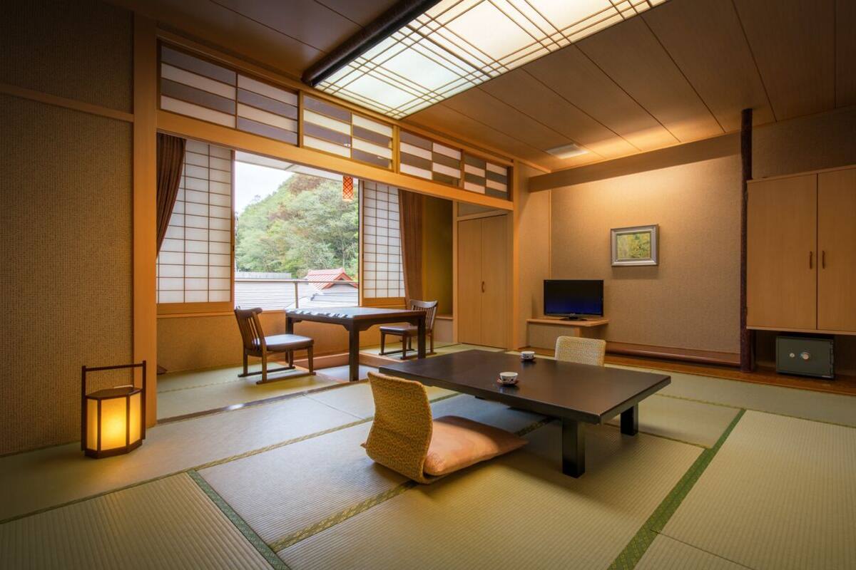 Une pièce de style japonais traditionnel, avec un sol recouvert de tatamis, une table basse, des chaises, un téléviseur et une porte coulissante.