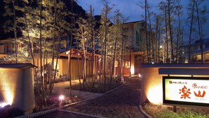 A pathway leading to a building surrounded by bamboo trees, with illuminated signs and a stone pathway.
