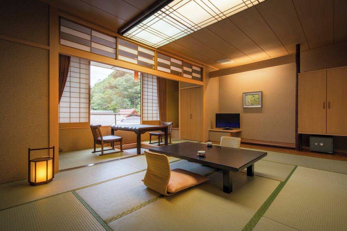 Une pièce de style japonais traditionnel, avec un sol recouvert de tatamis, une table basse, des chaises, un téléviseur et une porte coulissante.