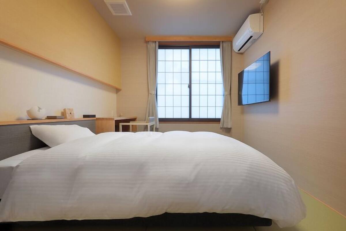 Une chambre d’hôtel avec un lit, une petite table, une chaise, une télévision et une fenêtre avec des rideaux.
