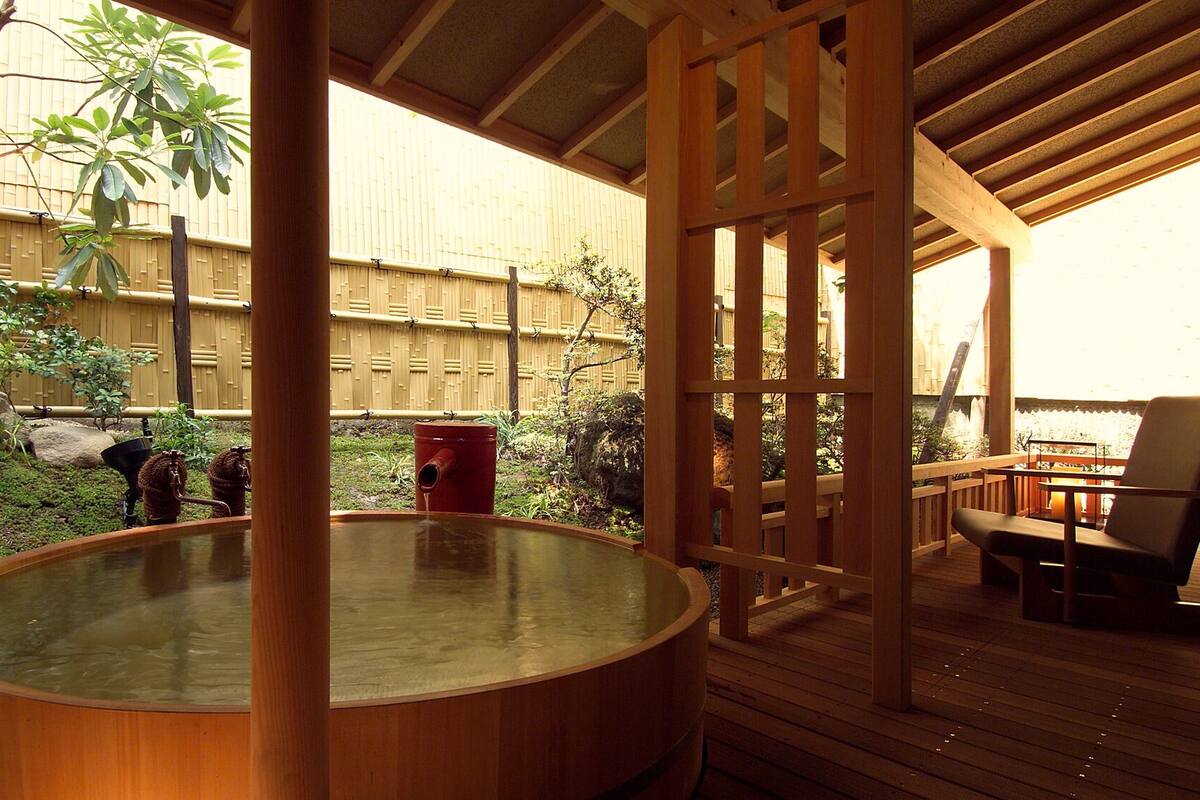 Un bain à remous installé sur une terrasse en bois, entouré d’une clôture en bambou, avec en arrière-plan une structure également en bambou.