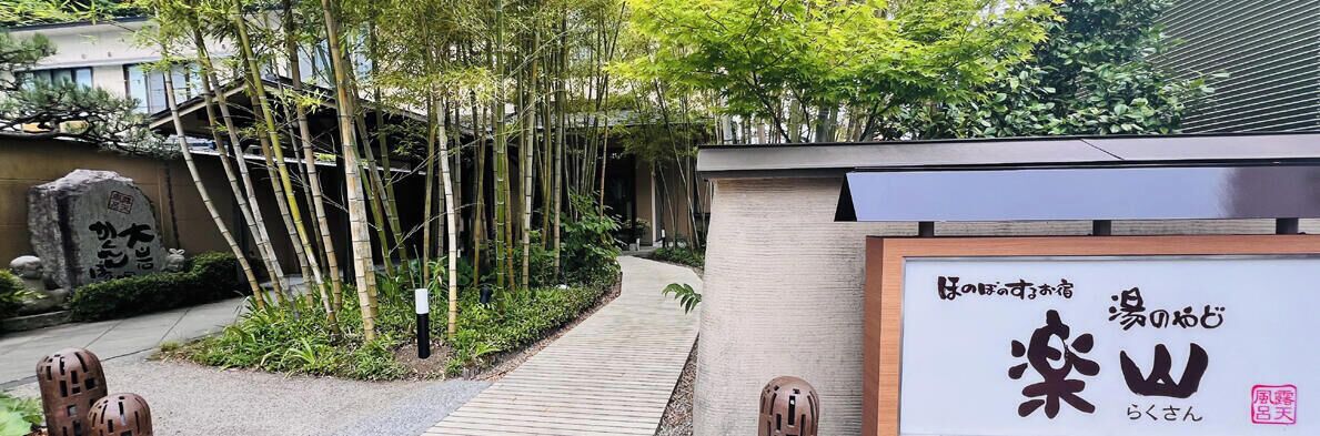 Ein traditionelles japanisches Gebäude mit einem hölzernen Pfad, Bambus und einem Schild mit japanischen Schriftzeichen.