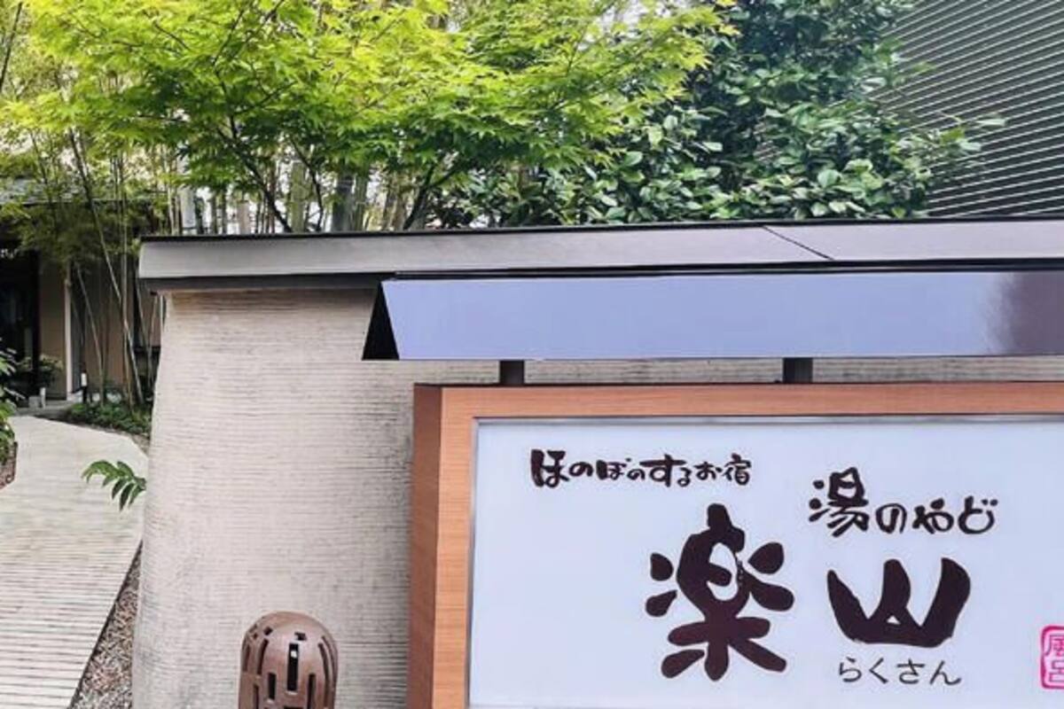 Un bâtiment traditionnel japonais avec un chemin en bois, des bambous et une enseigne ornée de caractères japonais.