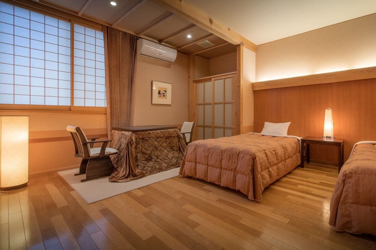 Une chambre d’hôtel avec un plancher en bois, deux lits, un bureau avec une chaise, une fenêtre avec des rideaux et un appareil de climatisation.