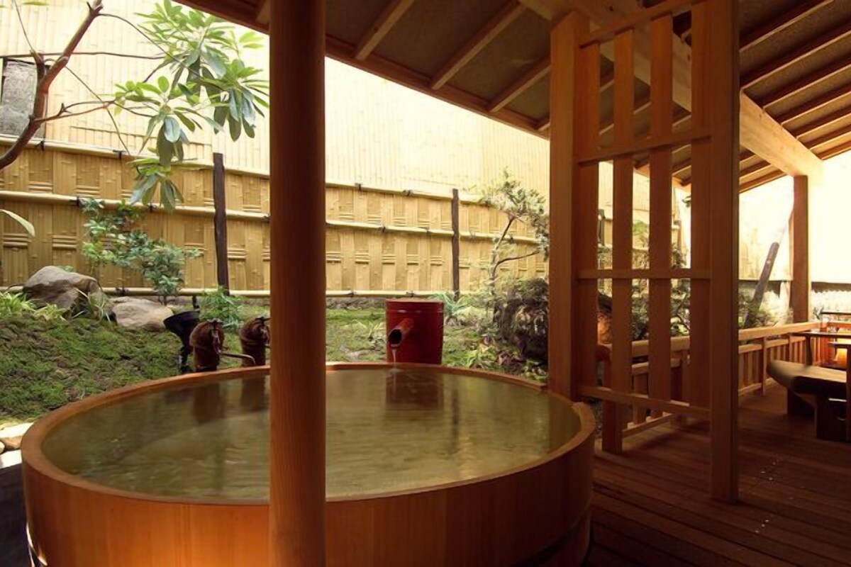 Un jacuzzi en un área de terraza de madera, con cerramiento de bambú y vista al jardín.