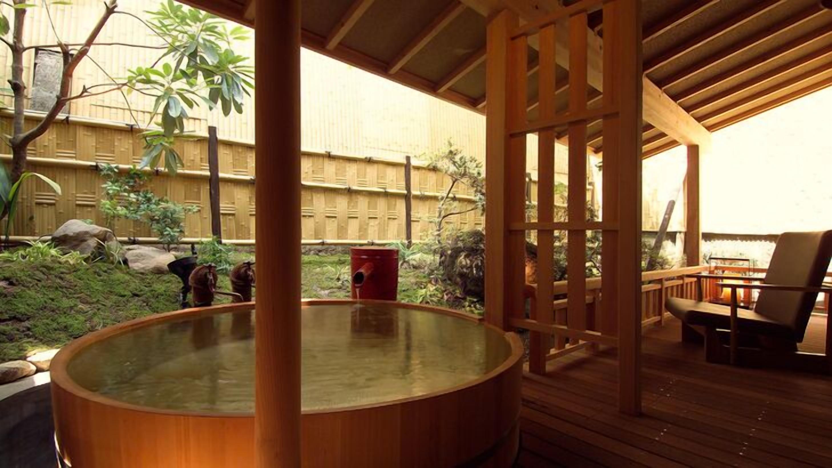 A hot tub in a wooden deck area with a bamboo fence and a view of the garden.