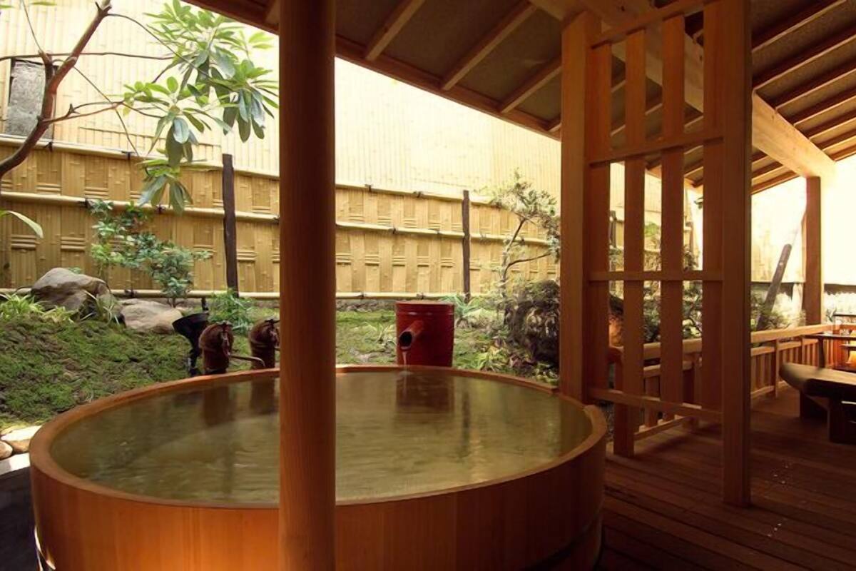 Un bain à remous installé sur une terrasse en bois, agrémentée d’une clôture en bambou et offrant une vue sur le jardin.