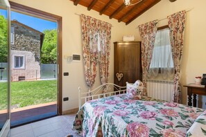 A bedroom with a bed, a wooden cabinet, a radiator, and a view of a stone building through a glass door. - Single Room in Green Setting with Wi-Fi and Workspace (Vicchio)