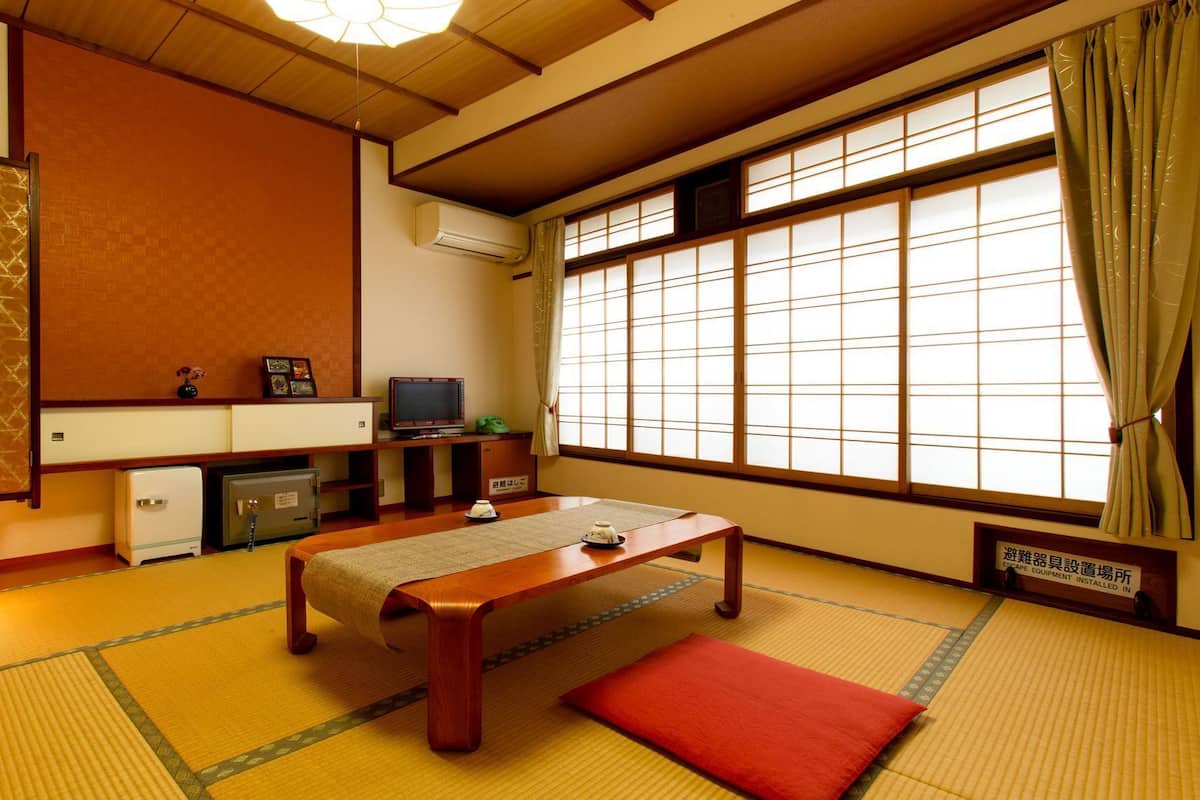 A traditional Japanese room with tatami flooring, a low wooden table, a television, and a futon bed.